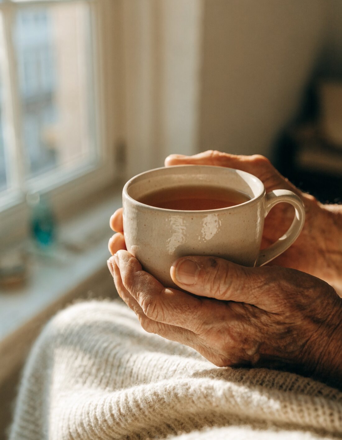 A resident enjoying a warm cup of tea by the window at Sunset Adult Family Home